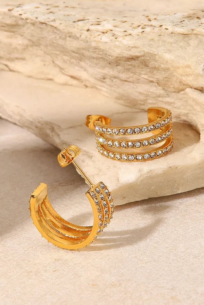Gold hoop earrings with embedded stones on a stone surface