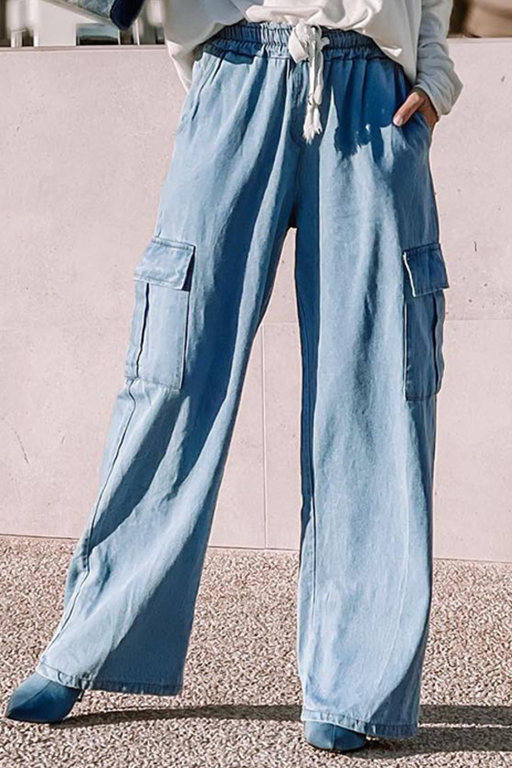 A pair of blue wide leg drawstring jeans with pockets, displayed on a person standing against a neutral background.