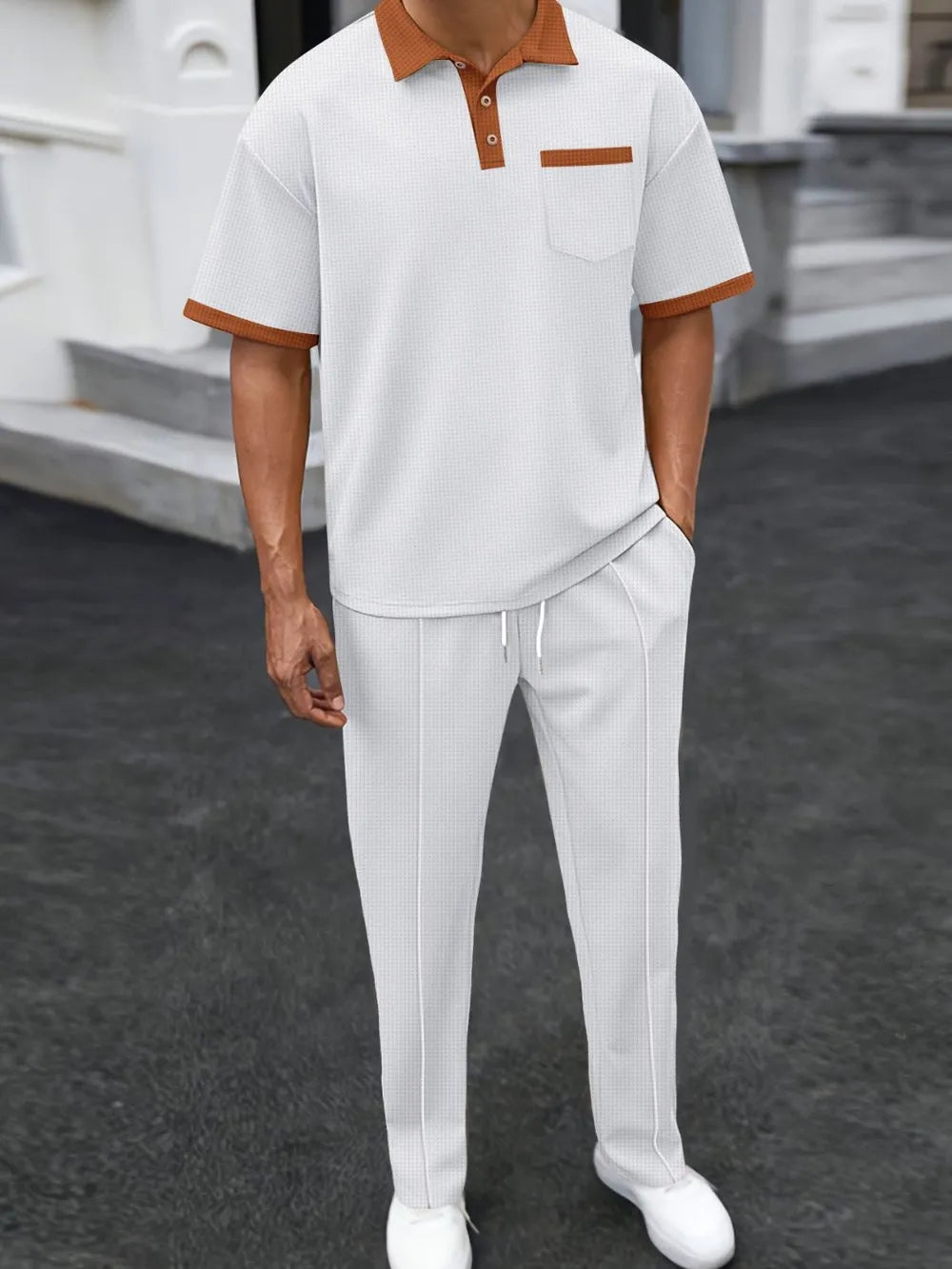 Person wearing a white polo shirt with brown accents and white pants on a dark surface.