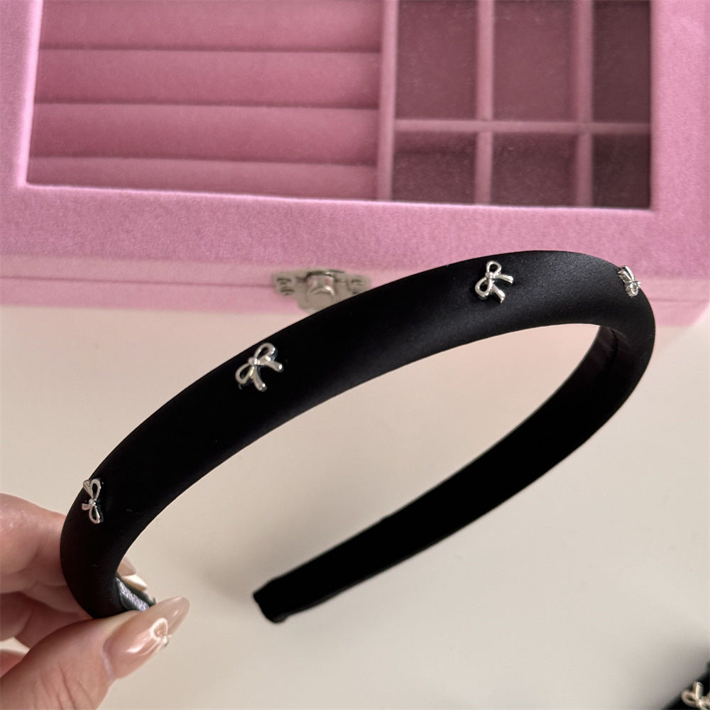 A sophisticated black padded headband detailed with a polished silver alloy bow accent.