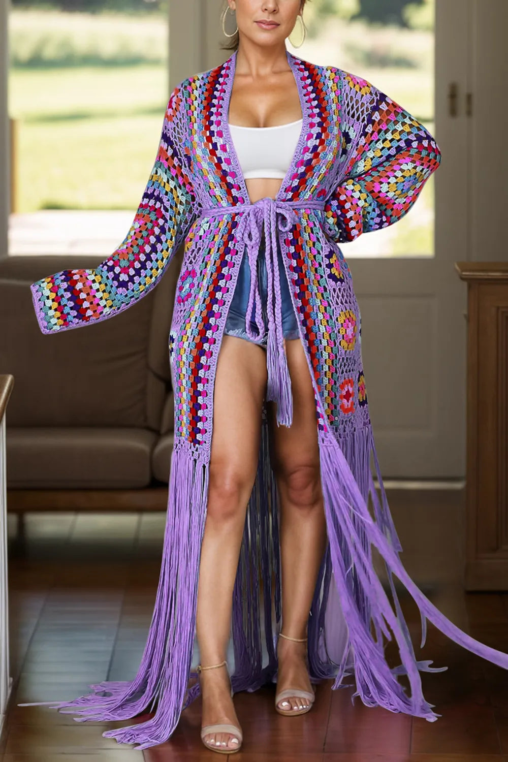 Woman wearing a colorful crochet cardigan with fringe in a room.