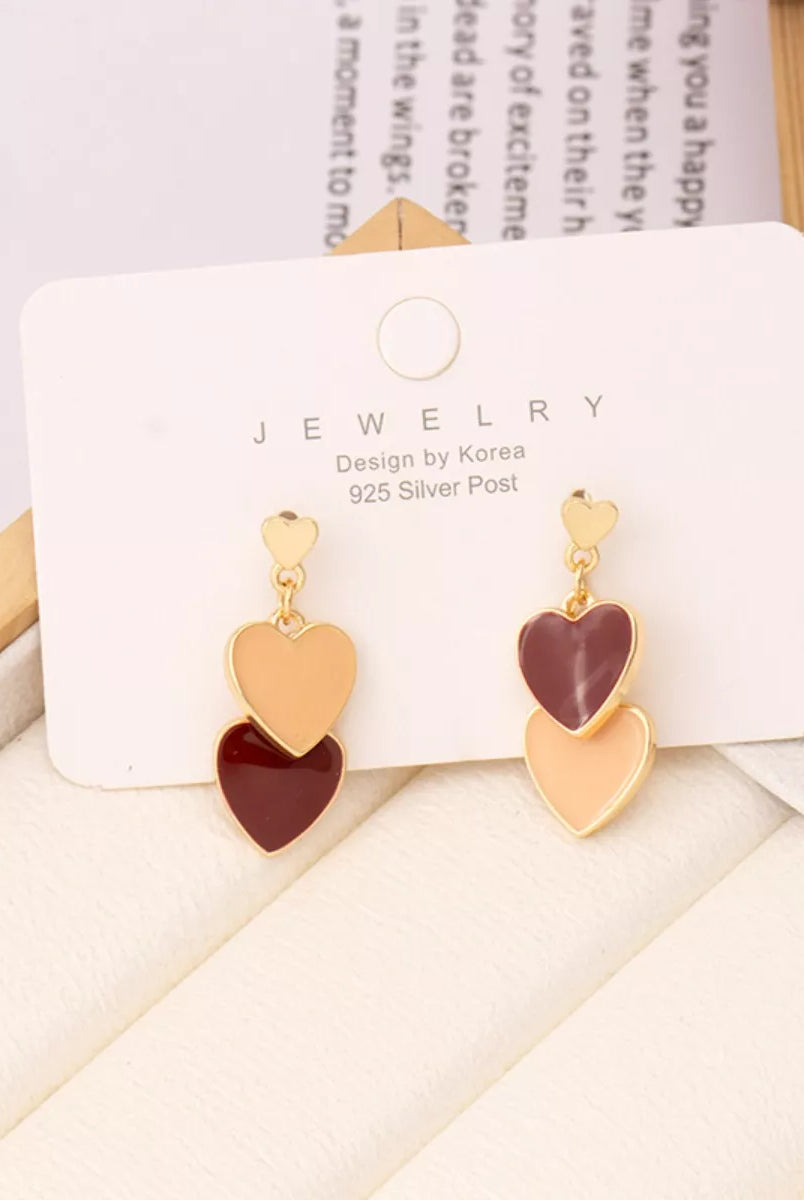 Heart-shaped earrings on a jewelry card with a wooden surface and book in the background