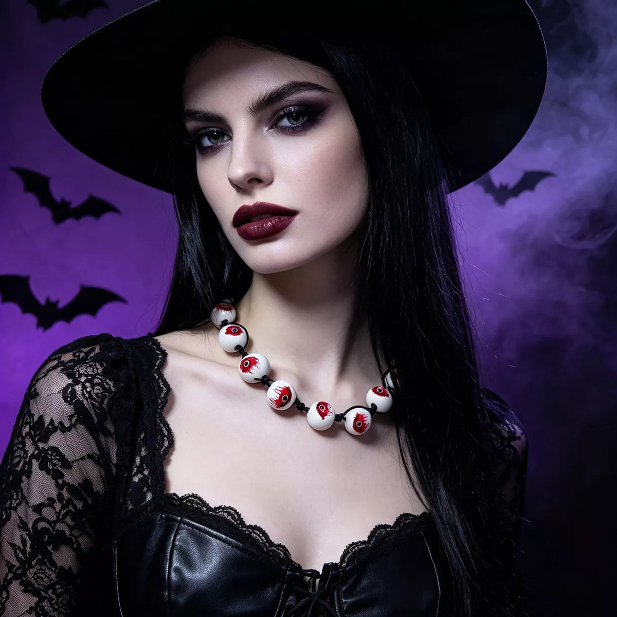 A woman in a black witch hat and black lace dress wears a necklace made of white beads with red blood-like details, posed against a purple smoky background with bat silhouettes.