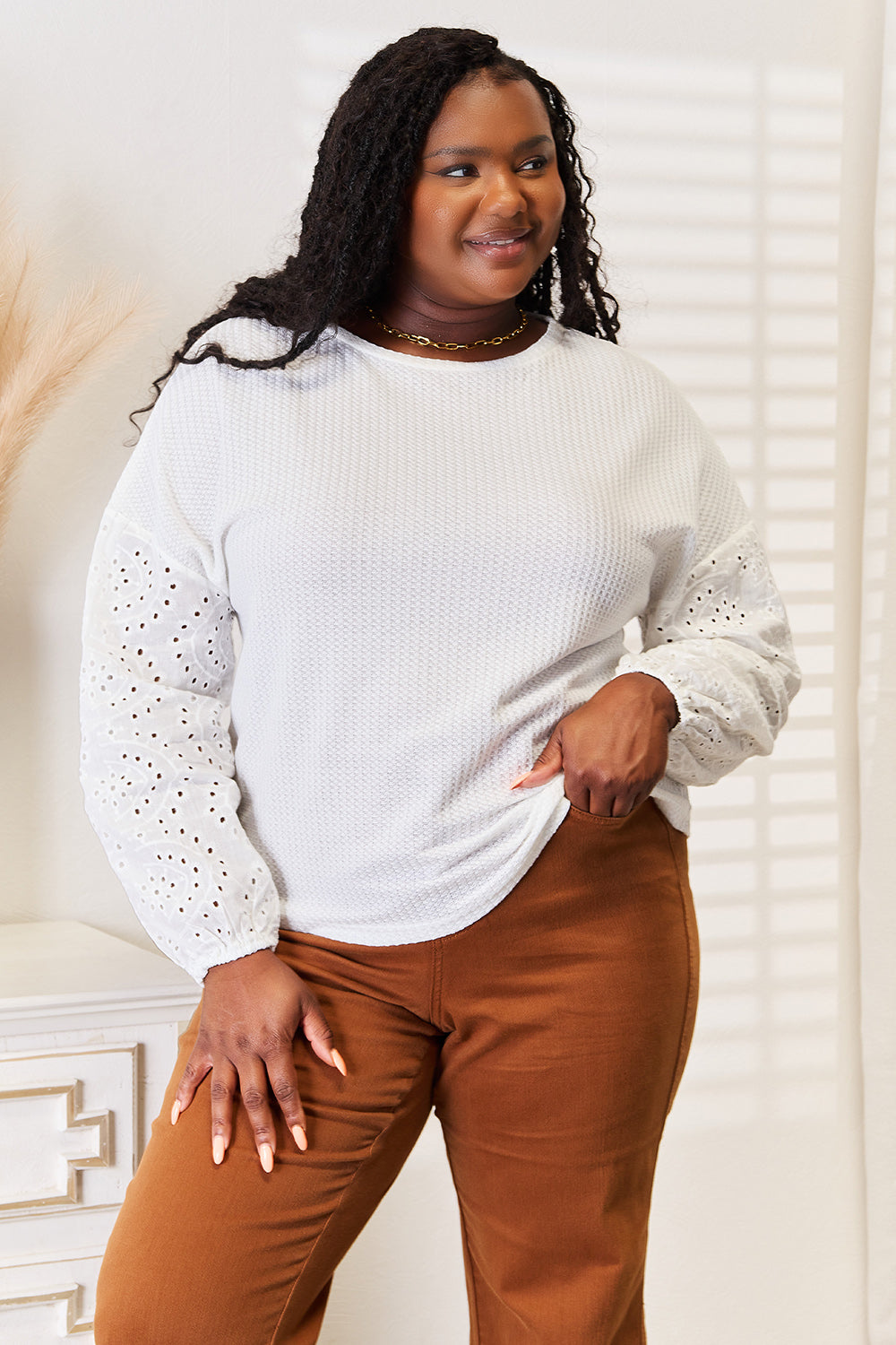 Woman wearing a light gray sweater with lace details and brown pants indoors.