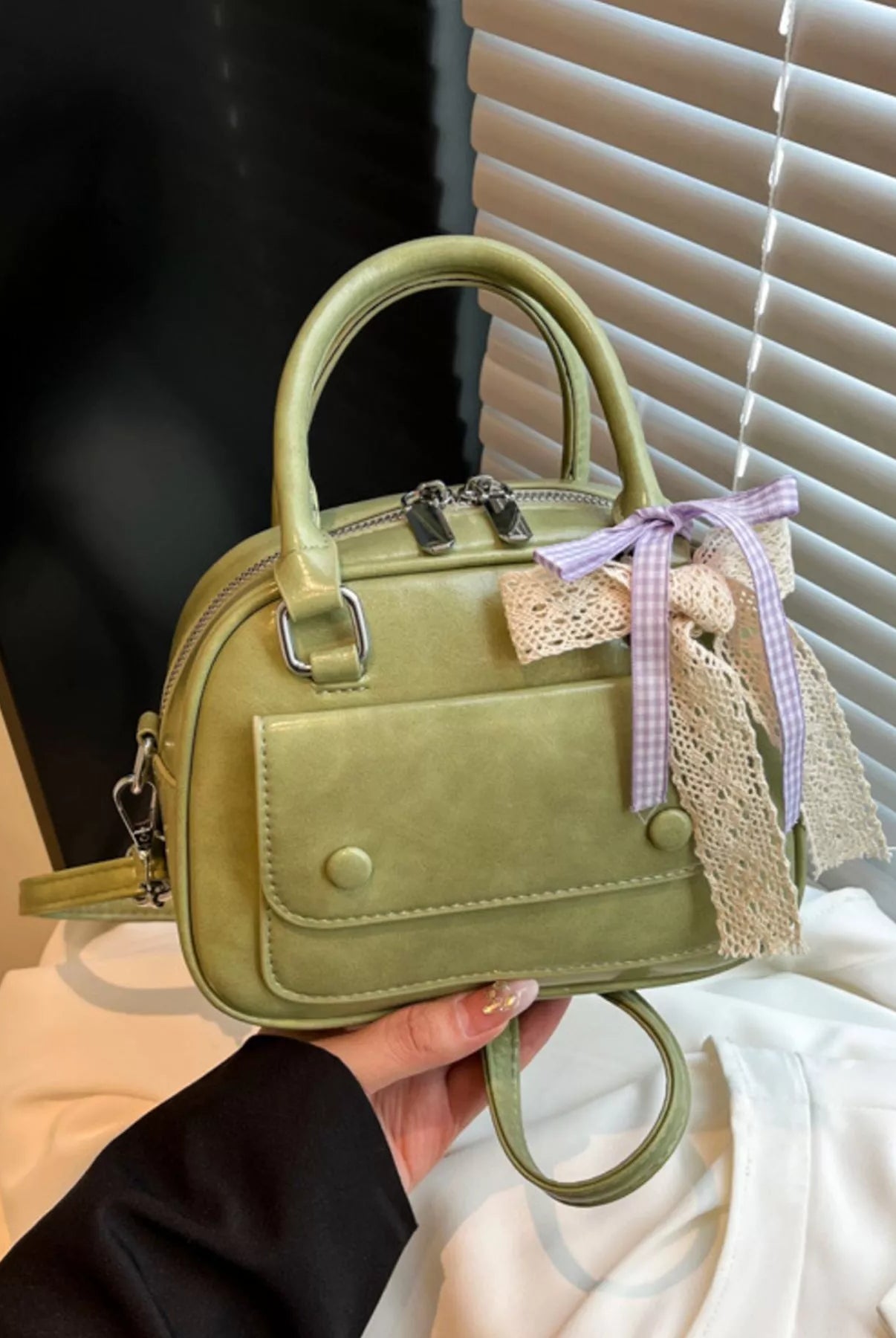 Green handbag with a decorative bow held by a person against a neutral background