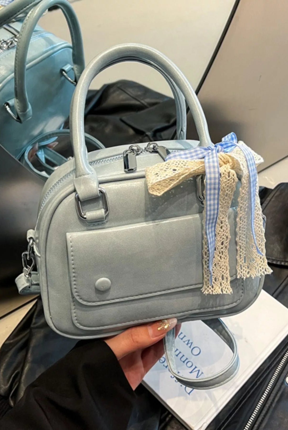 Gray handbag with decorative tassels held by a person, with a blurred background.