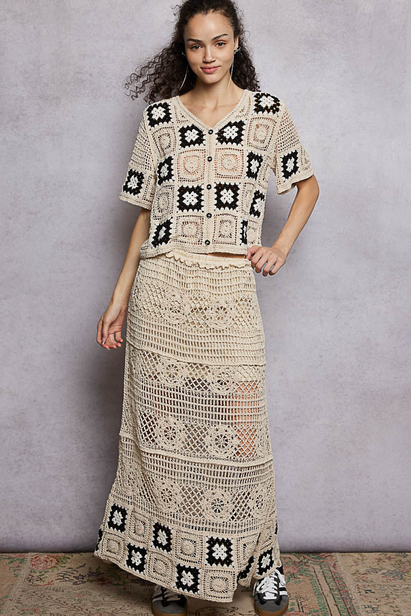Woman wearing a crochet outfit with a patterned top and long skirt against a plain background