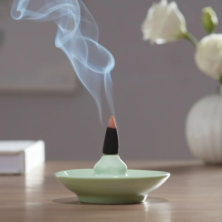 Incense cone burning on a green dish with smoke rising, placed on a wooden surface.