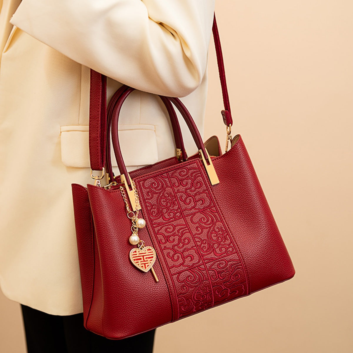 Red handbag with gold accents held by a person wearing a beige coat on a beige background