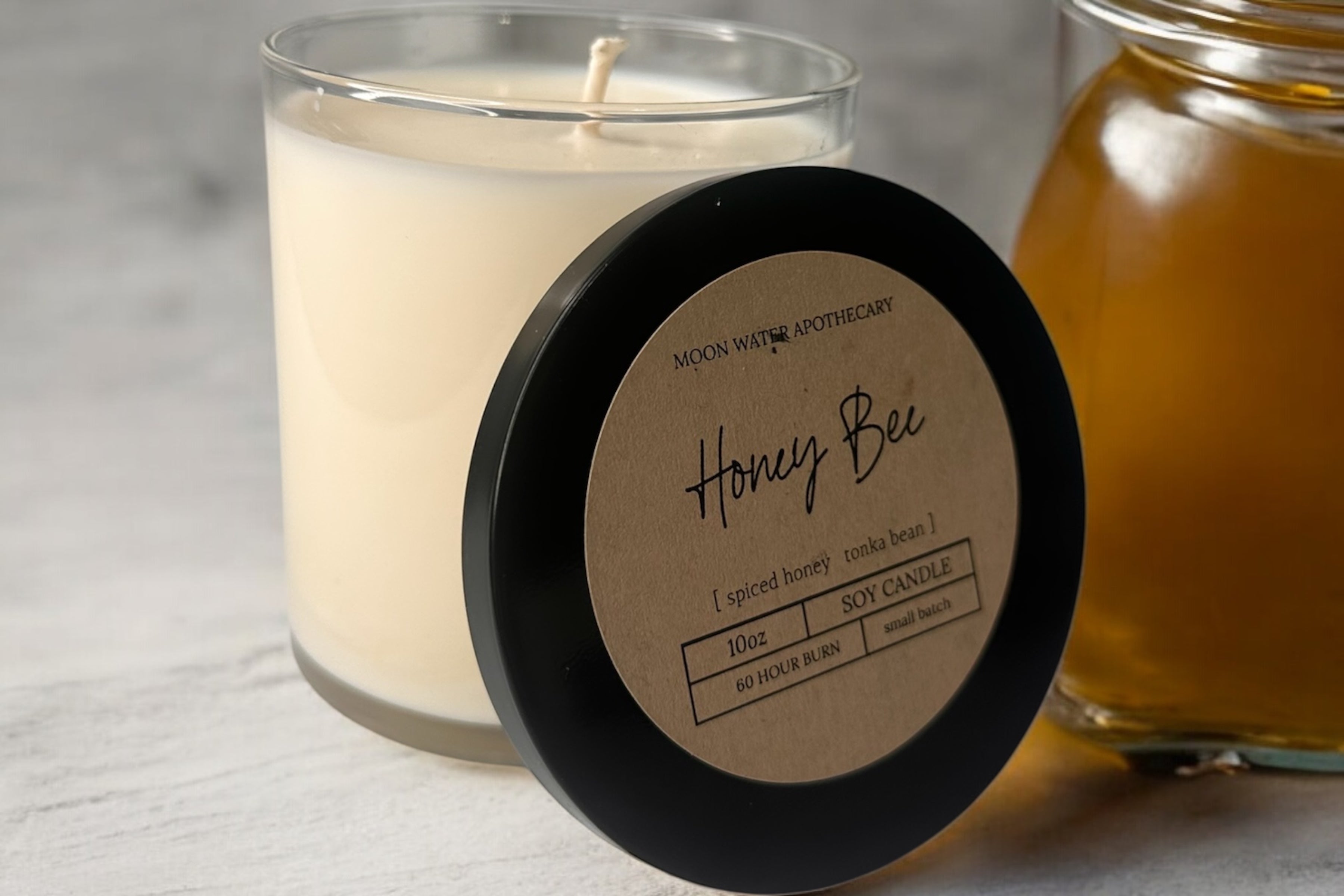 Candle labeled 'Honey Bee' with a jar of honey on a light background. Limited Edition Honey Bee Candle with a warm, golden honey scent. This expertly crafted candle delivers rich, comforting aromas that evoke natural meadows and blooming flowers. Enjoy hours of consistent, high-quality fragrance that brings inviting warmth to any room.