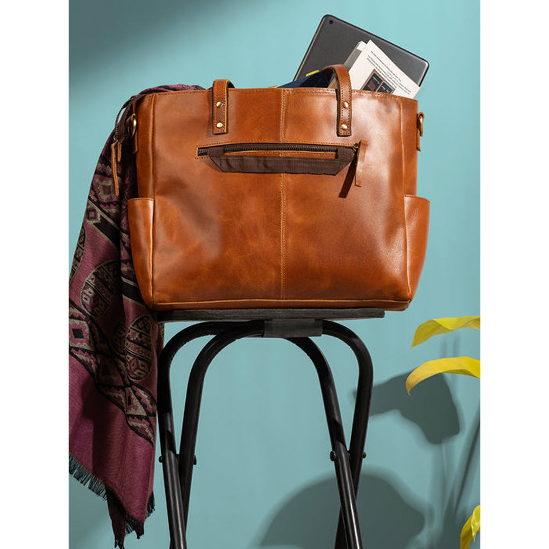 Brown leather bag with a laptop on a black stool against a teal background