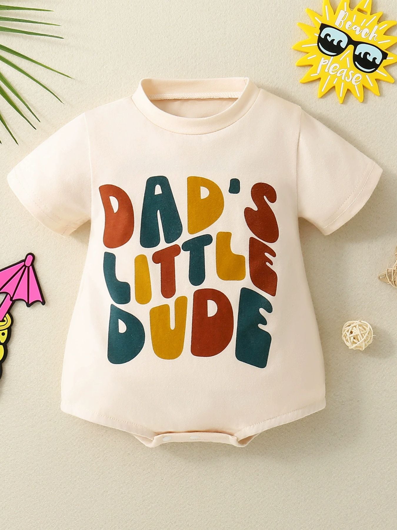 Beige t-shirt with colorful text 'DAD'S LITTLE DUDE' on a light background