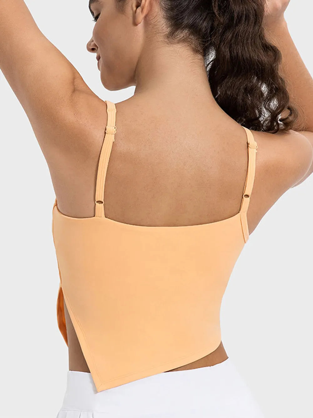 Woman wearing a peach-colored top with thin straps on a light gray background