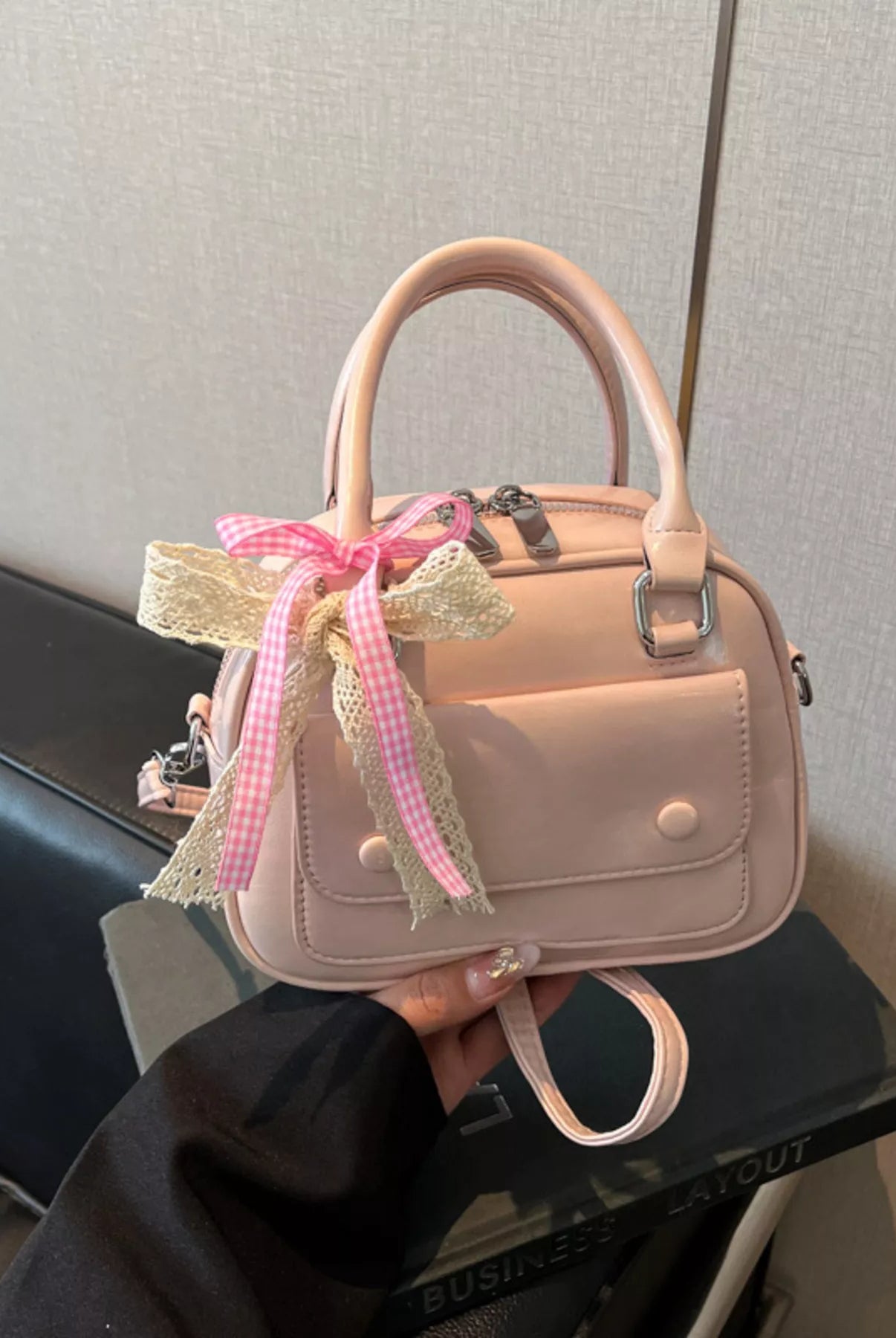 Pink handbag with a decorative bow held by a person against a neutral background