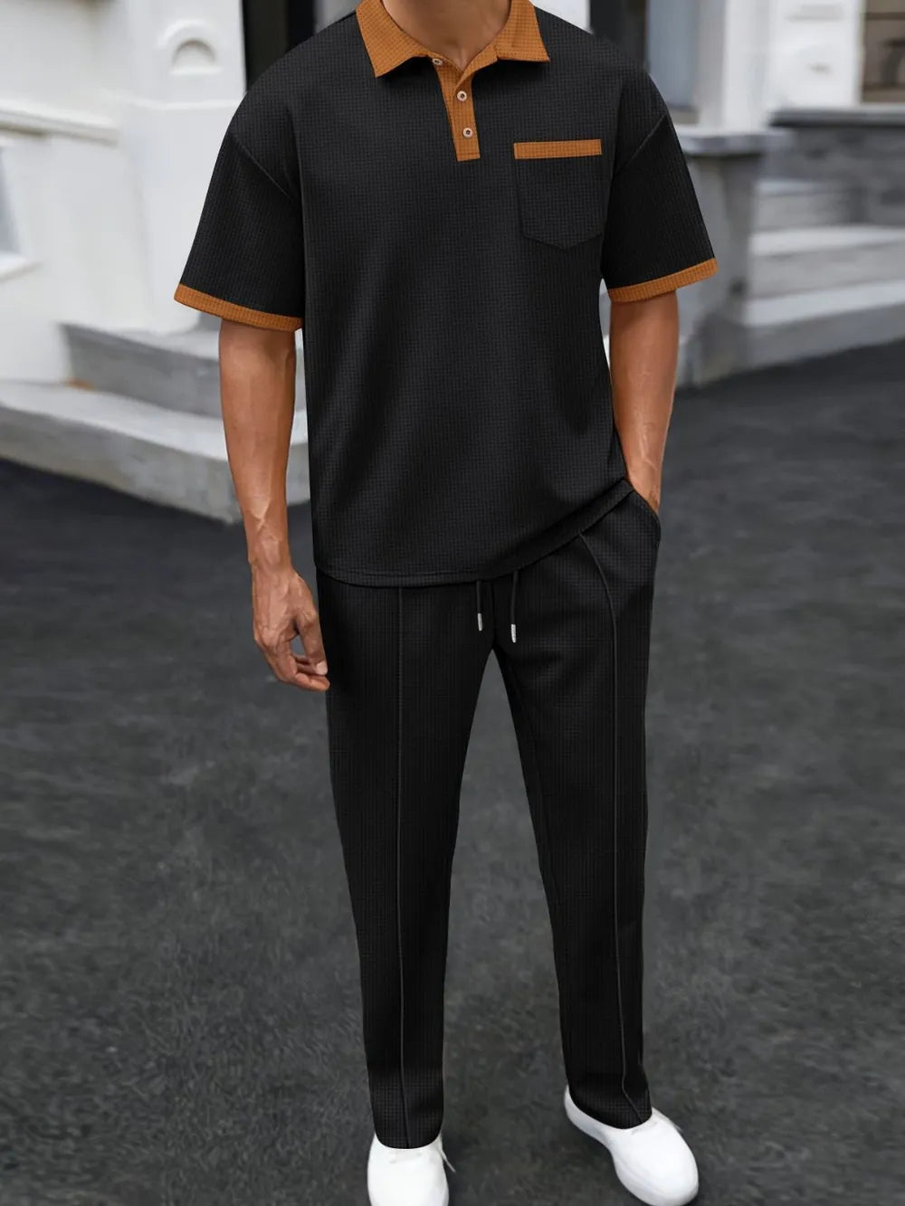 Person wearing a black and brown outfit with white shoes on a dark surface.