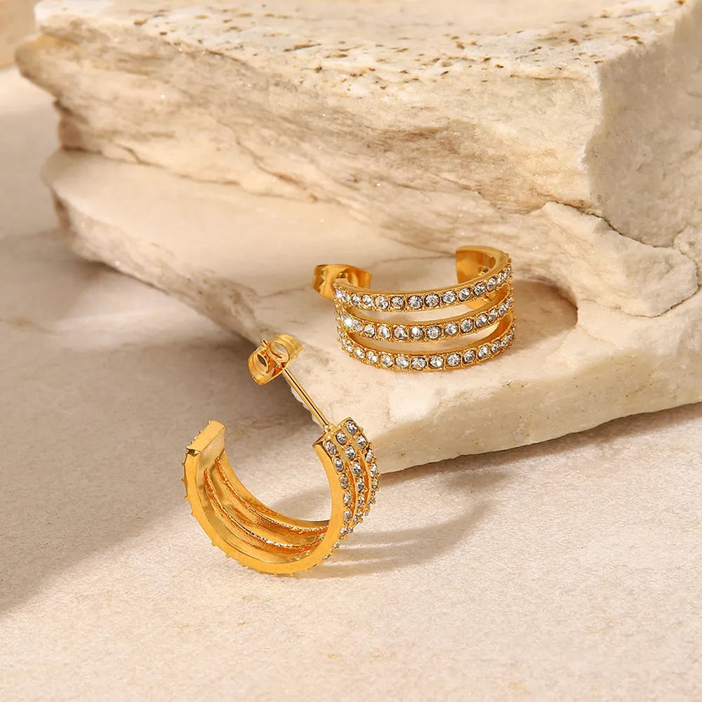 Gold hoop earrings with embedded stones on a stone surface