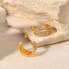 Gold hoop earrings with embedded stones on a stone surface