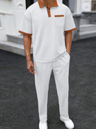 Person wearing a white polo shirt with brown accents and white pants on a dark surface.