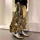 Person wearing a gold sequin skirt and silver boots in a room with white walls.