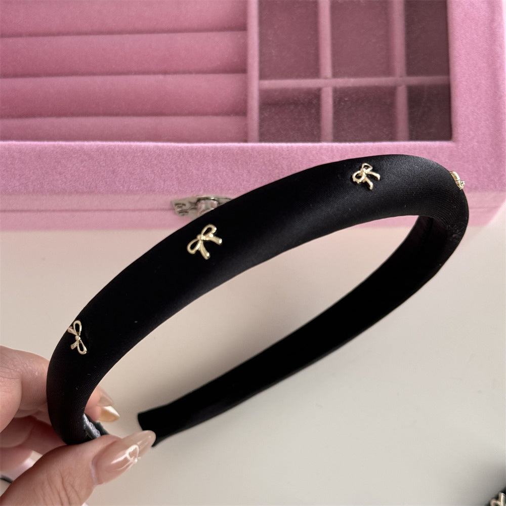 A luxury black padded resort headband detailed with an elegant gold alloy bow accent.