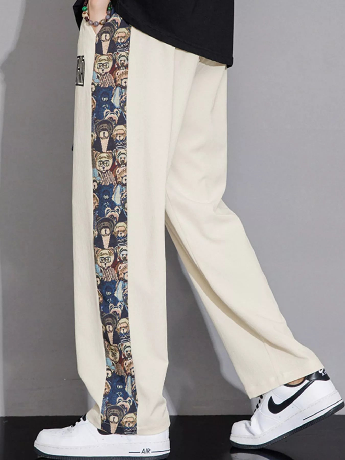 Beige pants with a colorful side stripe worn by a person, on a plain background