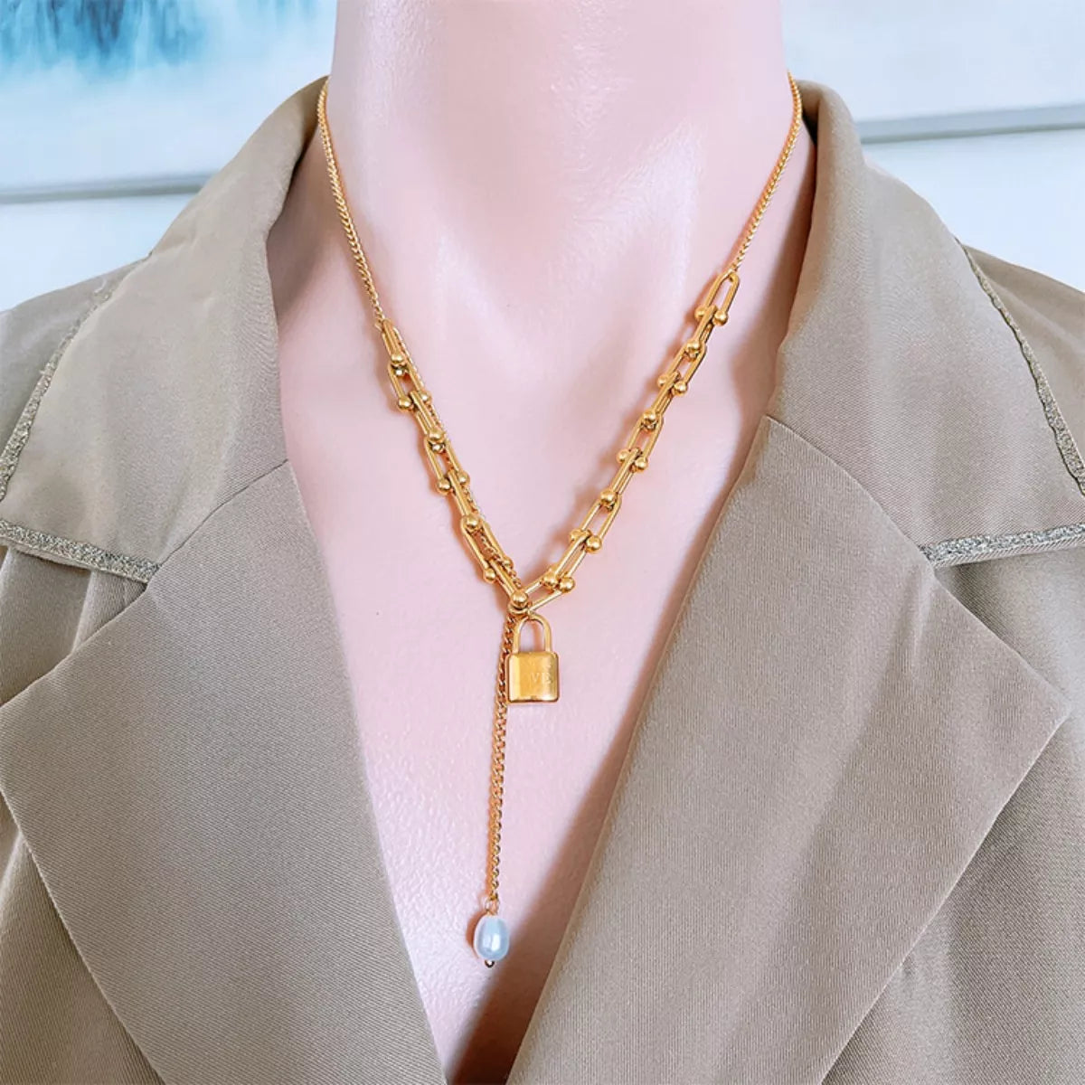 Gold necklace with a lock pendant on a person wearing a beige coat.