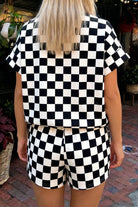 Back view of women's two-piece checkered luxury lounge set with a subtle geometric textured knit short-sleeve shirt and matching drawstring shorts in classic black.