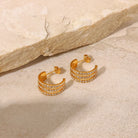 Gold hoop earrings with embedded stones on a stone surface