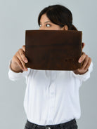 Person holding a brown leather clutch with a visible brand logo against a gray background