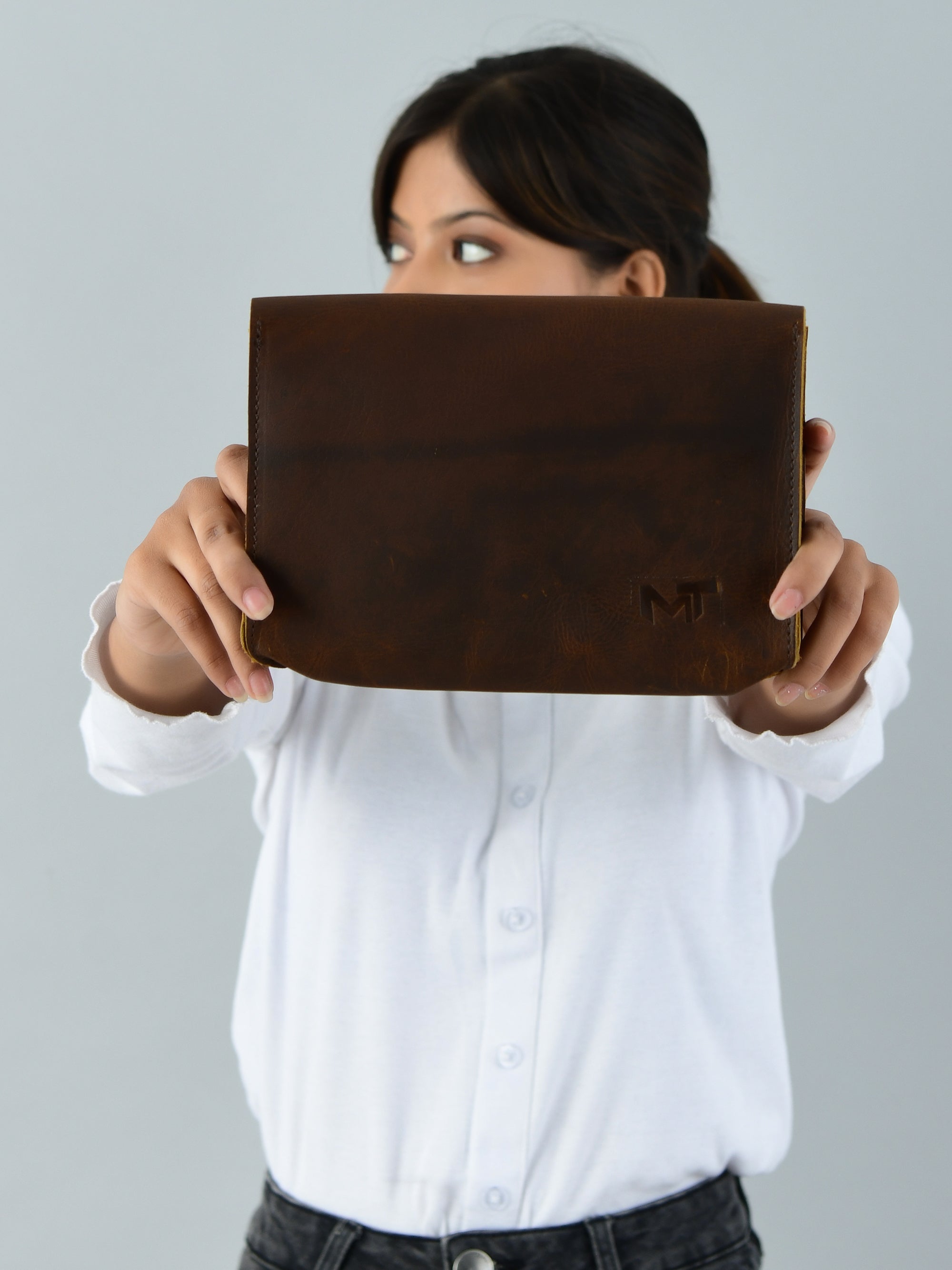 Person holding a brown leather clutch with a visible brand logo against a gray background