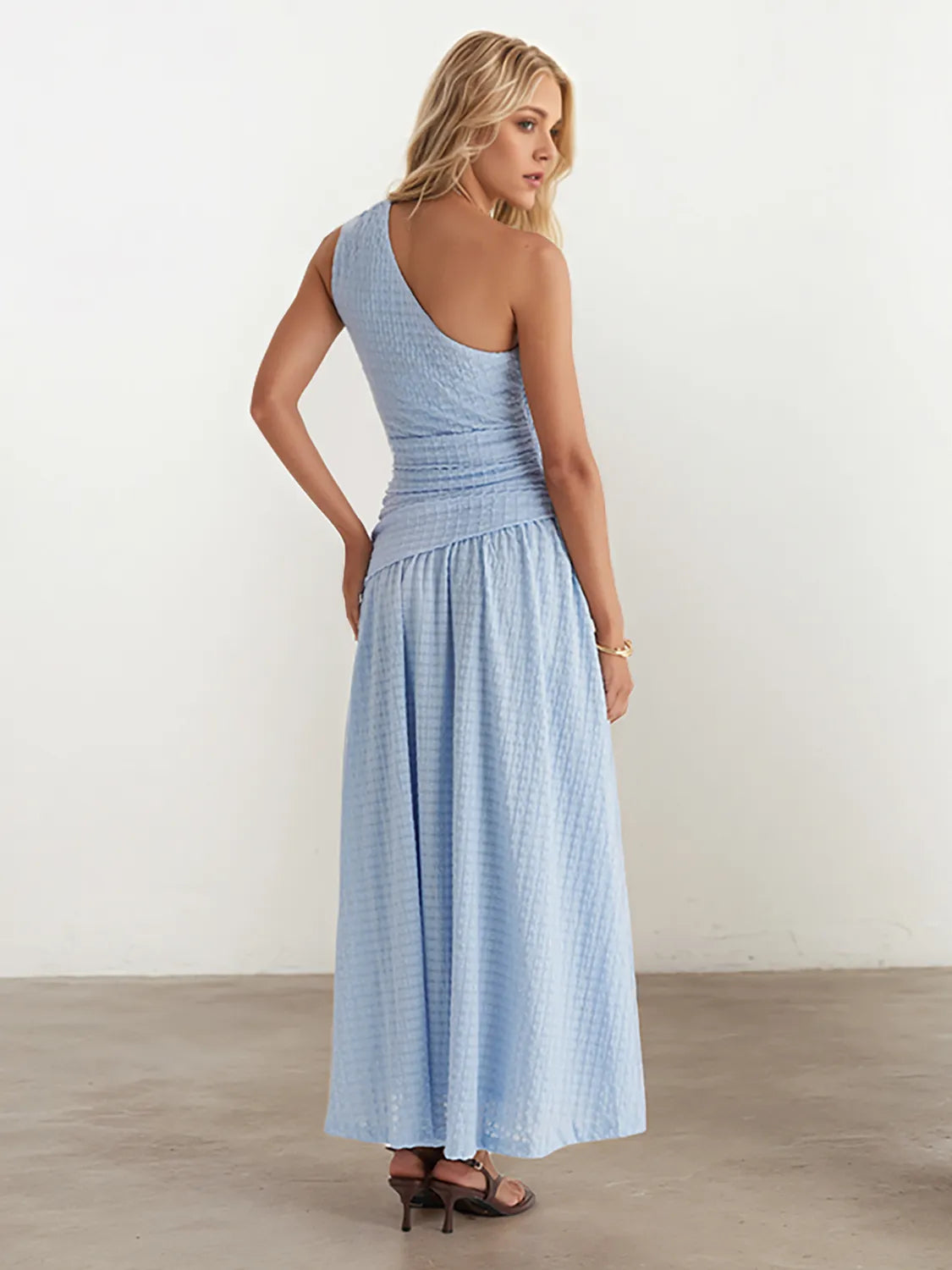 Woman wearing a light blue one-shoulder dress against a white background