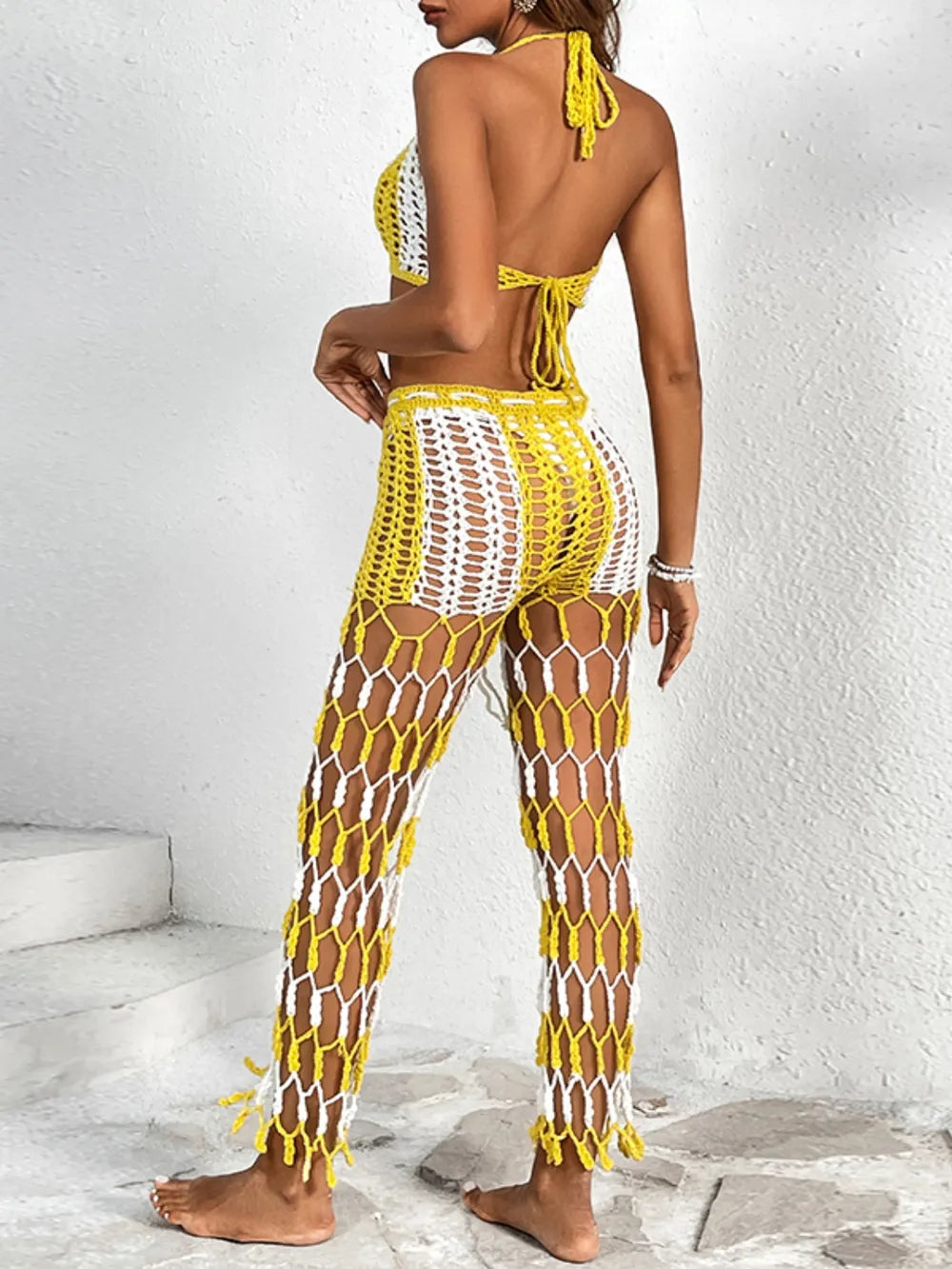 Woman wearing a yellow and white crochet outfit against a white wall.