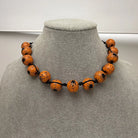 An orange beaded necklace with black spiderweb and spider designs, displayed on a gray fabric jewelry bust.