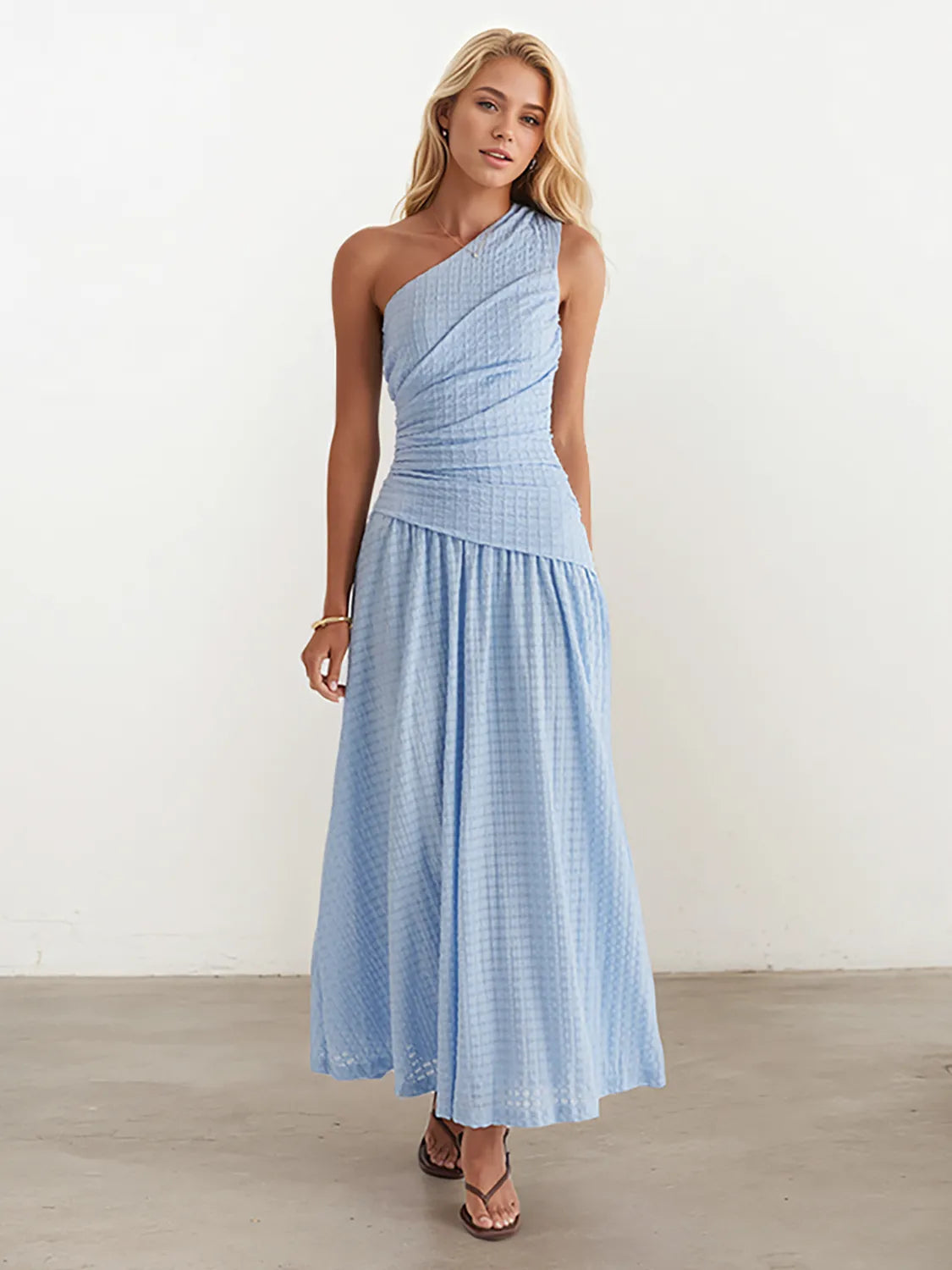 Woman wearing a light blue one-shoulder dress against a white background