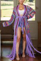 Woman wearing a colorful crochet cardigan with fringe in a room.