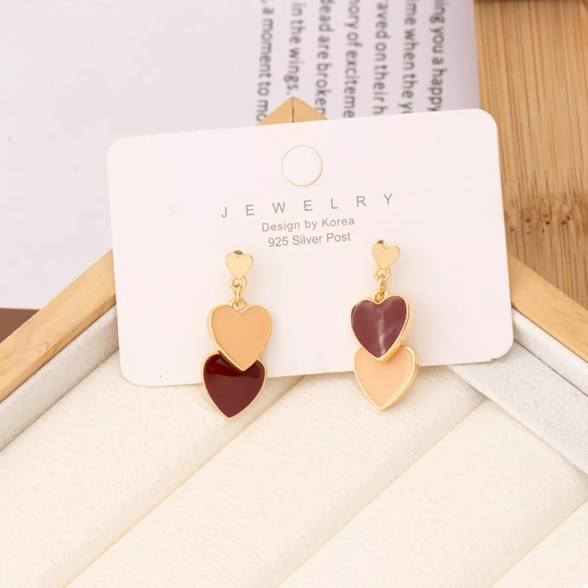 Heart-shaped earrings on a jewelry card with a wooden surface and book in the background