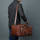 Person holding a brown leather suitcase against a gray background