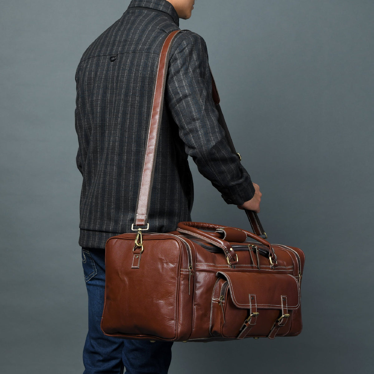 Person holding a brown leather suitcase against a gray background