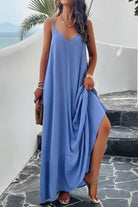 A woman wearing a  blue backless maxi cami dress with pockets, standing near a tropical setting.