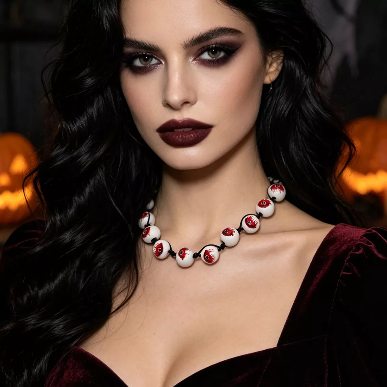 A woman with long dark wavy hair wears a beaded necklace made of white round beads with red and black details, photographed in a moody Halloween-themed setting with glowing jack-o'-lanterns in the background.