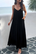 A woman wearing a black backless maxi cami dress with pockets, standing near a tropical setting.