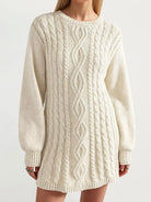 A woman wearing a cream-colored cable-knit sweater dress with a crew neck, long sleeves, and ribbed cuffs and hem, shown against a plain light background.