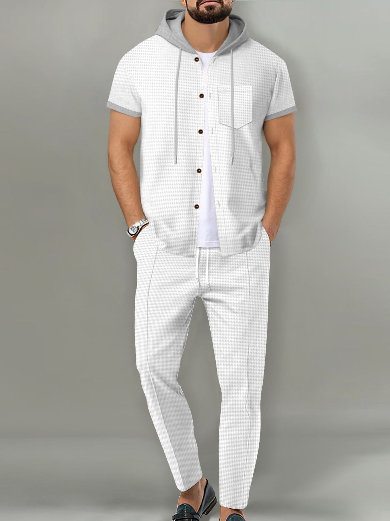 A man wearing a white short-sleeve button-front hooded shirt with gray trim and matching white pants, standing against a plain gray studio background.
