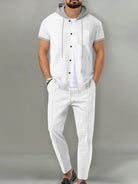 A man wearing a white short-sleeve button-front hooded shirt with gray trim and matching white pants, standing against a plain gray studio background.