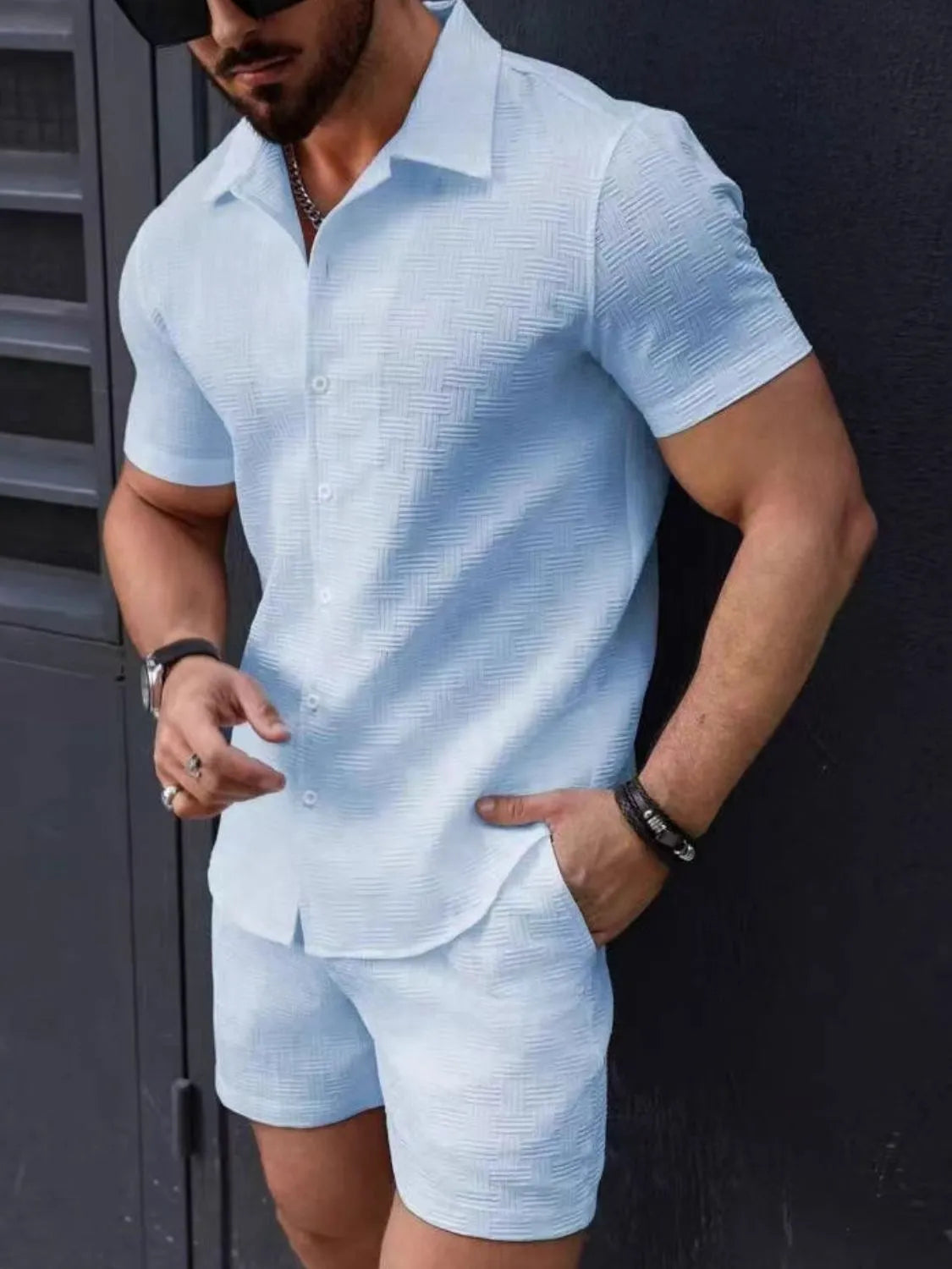 Man wearing a light blue textured shirt and shorts set against a dark background