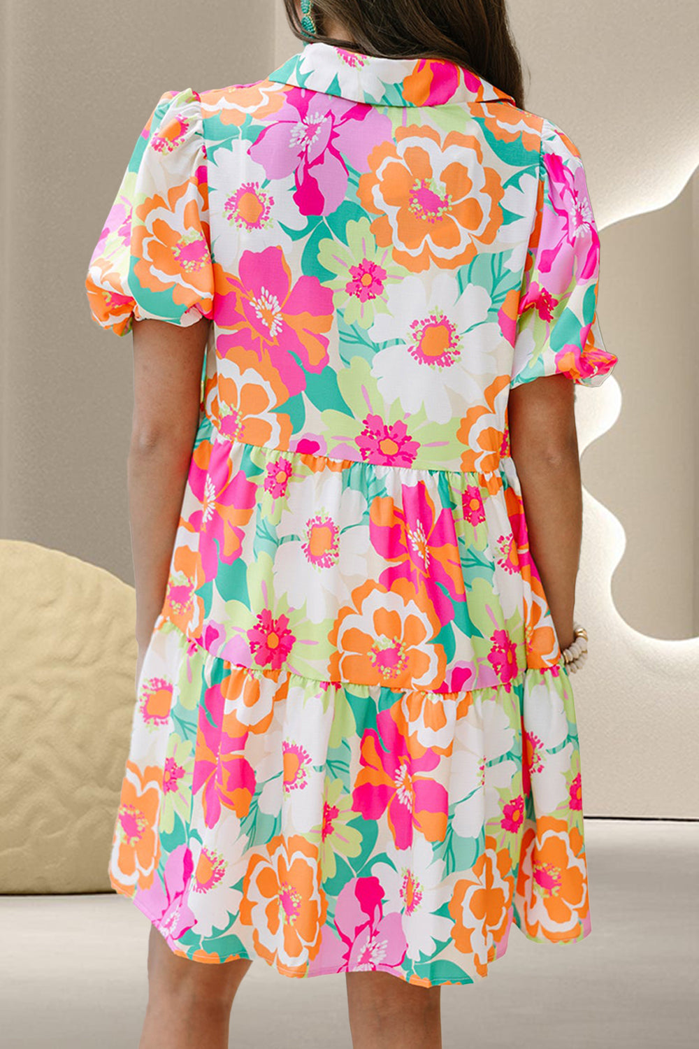 Back view of floral tiered mini dress with short puff sleeves and pink, orange, and green print.