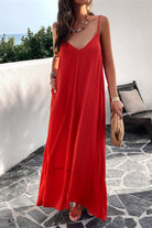 A woman wearing a red backless maxi cami dress with pockets, standing near a tropical setting.