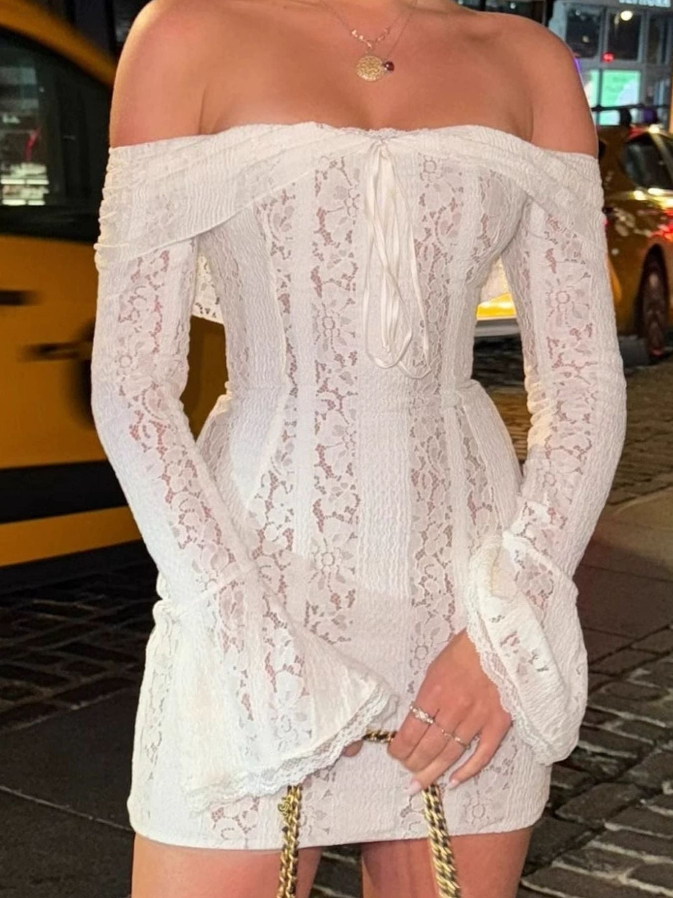 White lace off-shoulder dress worn by a person on a city street.