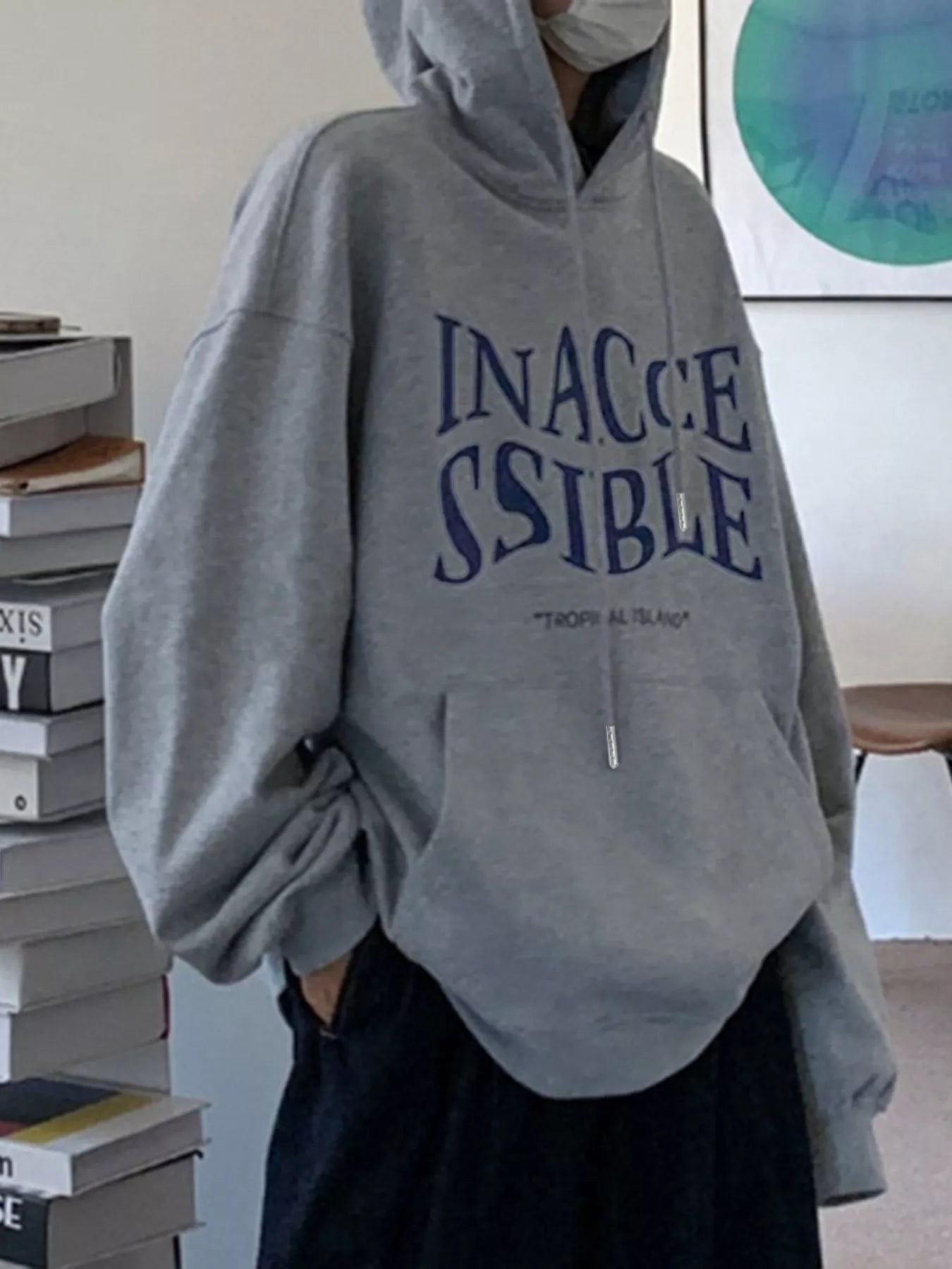 Person wearing a gray hoodie with 'INACCESSIBLE' text in blue, standing indoors.