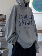 Person wearing a gray hoodie with 'INACCESSIBLE' text in blue, standing indoors.